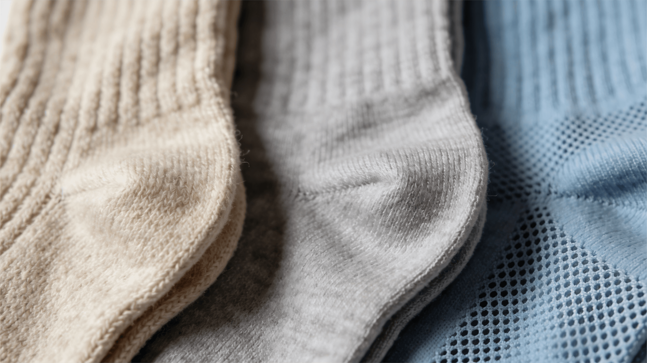 A macro close-up of three different sock textures: fuzzy Merino wool for winter warmth, smooth combed cotton for daily comfort, and breathable synthetic fabric for athletic performance and moisture-wicking.