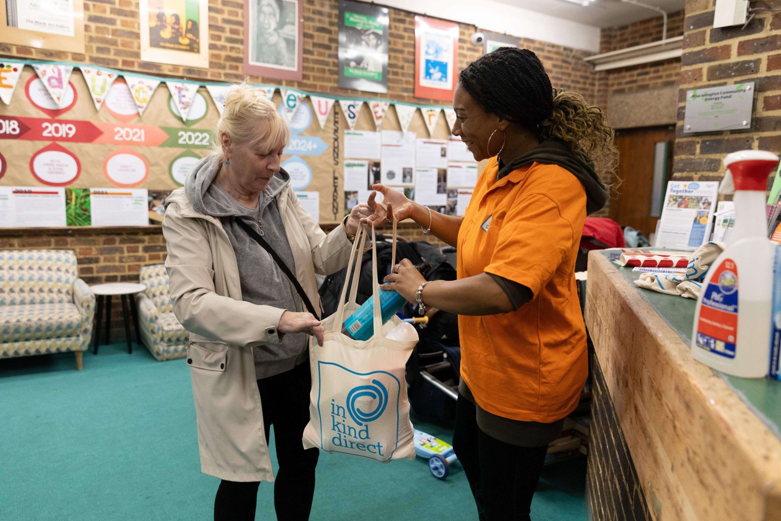 A community volunteer handing an In Kind Direct care package, including CloseMate essential clothing, to a local resident.