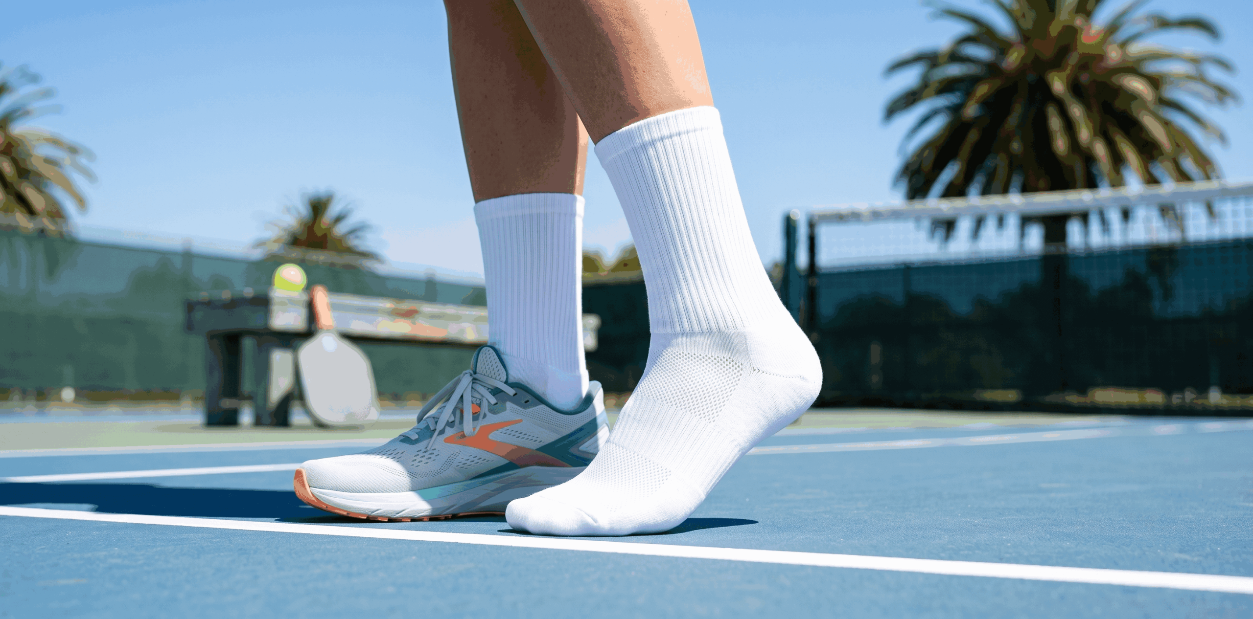 Woman wearing white performance crew socks and running sneakers on a sunny pickleball court